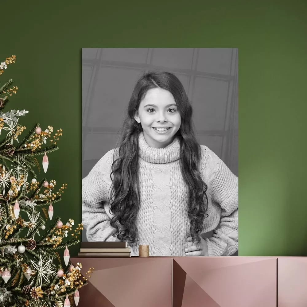 Een zwart-wit portret van een meisje, het portret hangt tegen een groene muur naast een kerstboom